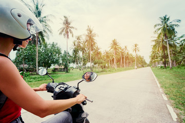 Tropical travel and transport. Happy young woman in helmet riding scooter on the road with palm trees. © luengo_ua