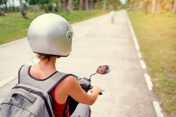 Fototapeta na wymiar Tropical travel and transport. Woman in helmet riding scooter on the road.