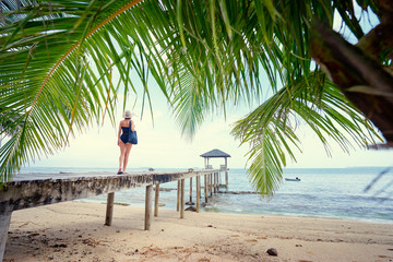 Enjoying suntan and vacation. Young woman in swimwear and hat standing on the wooden beach pier.