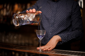 Barman pouring strong and fresh summer drink into the cocktail glass