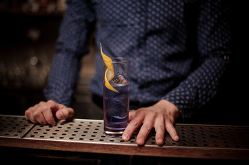 Barman with a glass of violet cocktail decorated with an orange pill