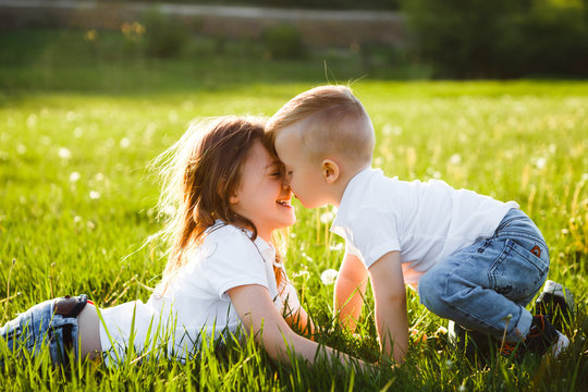 Sister and brother kiss each other lying on green grass.