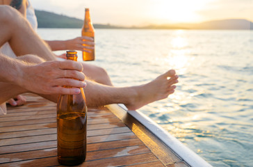 Party with friends. Close up male hand holding bottle of beer on the yacht sailing the sea.