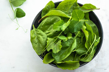 Fresh spinach in a black bowl on a white background. Top view.