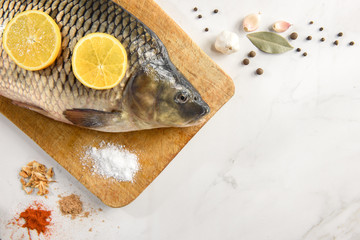 Raw fresh fish (carp) with lemon, garlic and spices on wooden cutting board on light vintage background with copy space. Healthy food and cooking.