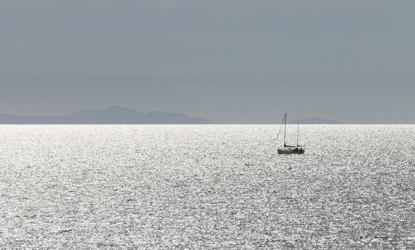 landscape image of a yacht on sparkling ocean water with land on the horizon against a clear blue sky with copy space