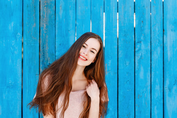 human emotion. portrait of a young cheerful girl with long hair on a blue wooden background. the model smiles cheerfully and looks into the camera.