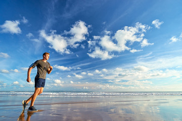 Fototapeta na wymiar Sports lifestyle. Happy young man in earphones jogging on the sea shore.
