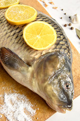 Raw fresh fish (carp) with lemon, garlic and spices on wooden cutting board on light vintage background with copy space. Healthy food and cooking.