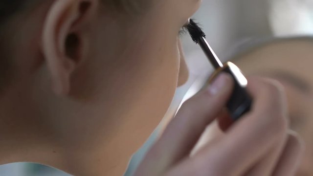 Young woman applying mascara close-up, morning make-up routine before work