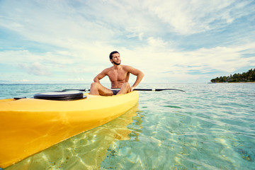 Young strong man kayaking in the sea near the tropical island. Adventure by kayak.