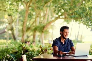 Freelance concept. Young  bearded man using laptop while sitting on summer terrace.