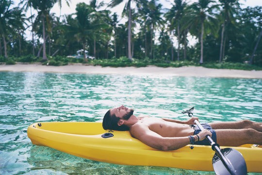 Young man relaxing and tanning the sea kayak in the tropical calm lagoon.