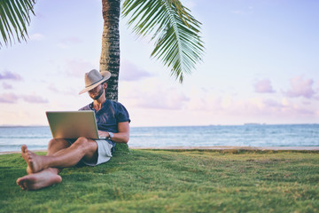 Work and vacation. Young man working on laptop computer on the tropical beach under the palm tree.
