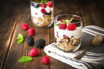 White yogurt with muesli and raspberries in glass bowls on rustic wooden background.