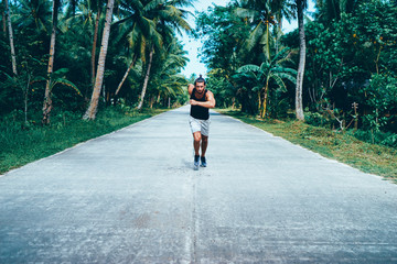 Healthy lifestyle. Jogging outdoors. Young strong man is running under palm trees.