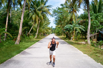 Fototapeta na wymiar Healthy lifestyle. Jogging outdoors. Young strong man is running under palm trees.