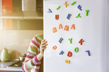 Woman looking in open fridge with Mama letters on door. Cooking for family and children concept