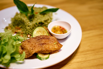 Green rice with fried fish, vegetables and sauce on wooden table.