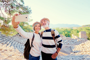 Tourism and technology. Traveling senior couple taking selfie together against ancient sightseeing background.
