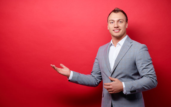 Advertisement. Colorful studio portrait of young handsome businessman pointing copy space. Red background.