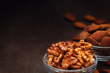 Close up bowl of almonds and walnuts on a dark background. Dried fruit to lower cholesterol. Negative space to write. Front view.