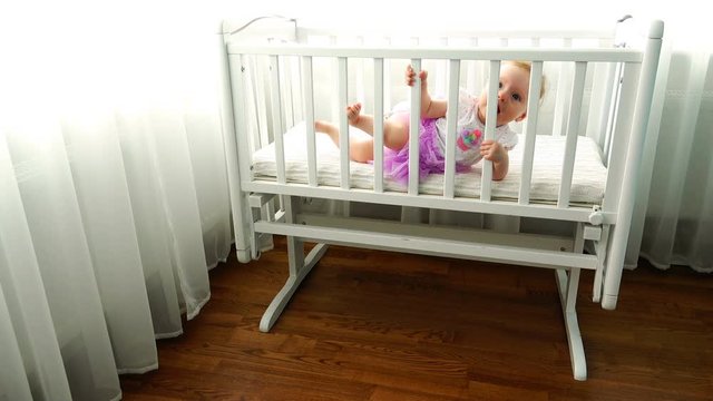 a child leans on the side of a white child's cot in the bedroom.