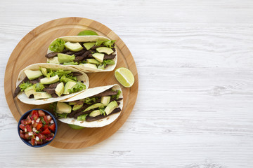 Corn tortillas with grilled beef, avocado, lime and salsa on wooden board. Top view. Copy space and...