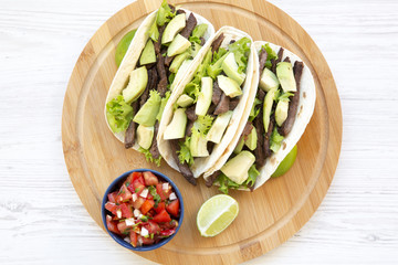 Top view corn tortillas with grilled beef, avocado, lime and salsa on wooden board. From above.