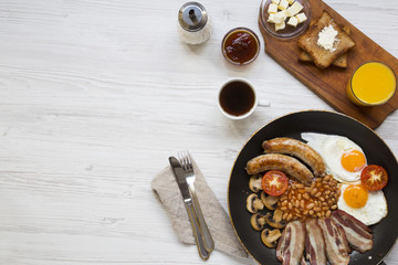 Full English breakfast in a pan with fried eggs, bacon, beans, sausages  and toasts on white wooden background, top view. Copy space. Flat lay. From above.