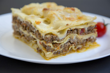 Traditional lasagne on a white plate. Dark background. Side view. Closeup.