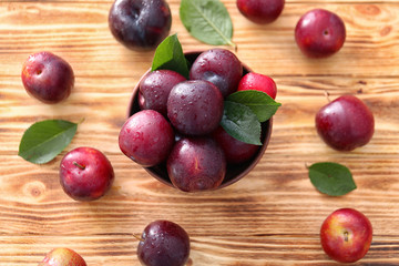 Bowl with ripe juicy plums on wooden table