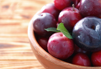 Bowl with ripe juicy plums on table, closeup