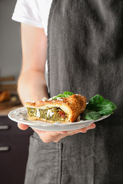 Woman holding piece of tasty pie with spinach on plate