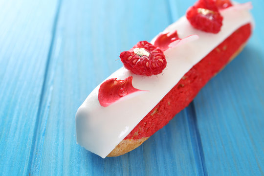 Tasty eclair with raspberry on wooden background