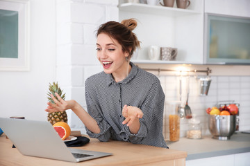 Young blogger with fruits and laptop on kitchen