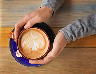 Woman holding cup of aromatic coffee with foam at wooden table, top view