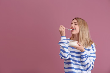 Young attractive woman eating tasty yogurt on color background