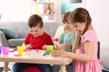 Cute little children using play dough at table indoors