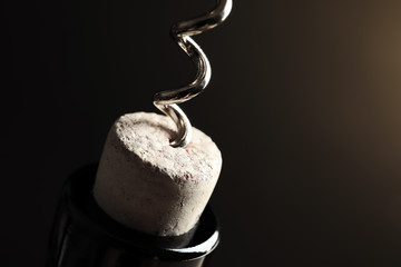 Opening bottle of wine with corkscrew on dark background, closeup