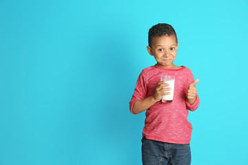 Adorable African-American boy with glass of milk on color background
