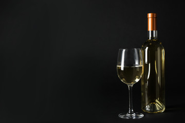 Bottle and glass of expensive white wine on dark background