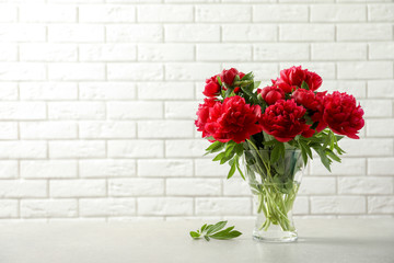 Fototapeta na wymiar Vase with beautiful blooming peonies on table near brick wall