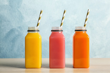 Bottles with tasty juices on table against color background