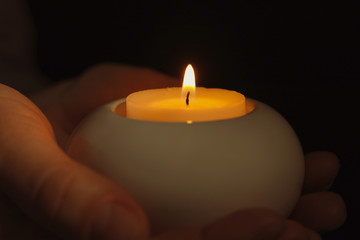 Young person holding burning candle in darkness, closeup
