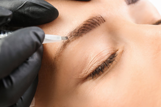 Young woman undergoing eyebrow correction procedure in salon