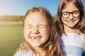 Two joyful girls hugging and closed their eyes from the sun. Sincere emotion. Girls without front teeth.