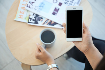 Young woman with cup of coffee holding mobile phone in hand at table indoors