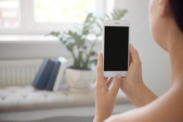 Young woman holding mobile phone with blank screen in hands indoors