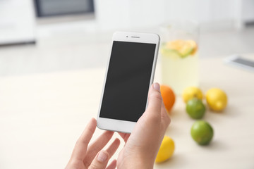 Young woman holding mobile phone with blank screen in hands indoors